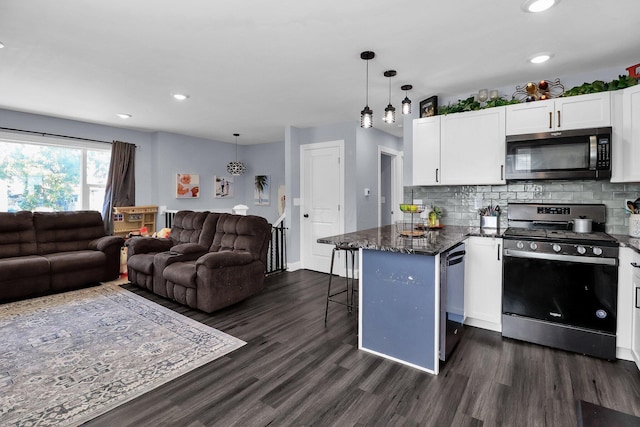 kitchen with appliances with stainless steel finishes, white cabinetry, a kitchen bar, hanging light fixtures, and kitchen peninsula