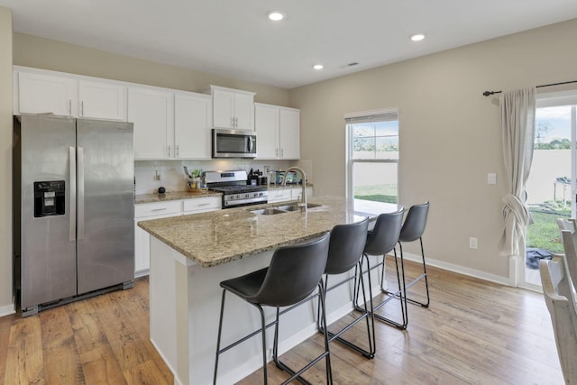 kitchen with light stone counters, stainless steel appliances, sink, a center island with sink, and white cabinetry