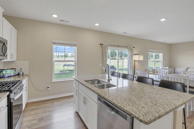 kitchen with a kitchen bar, appliances with stainless steel finishes, sink, white cabinets, and an island with sink