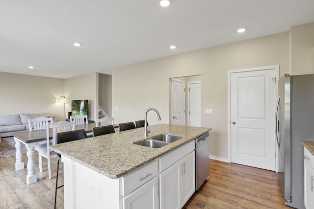 kitchen featuring stainless steel appliances, sink, white cabinets, a breakfast bar area, and an island with sink