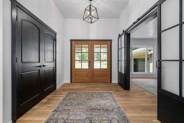 entryway with a barn door, french doors, a notable chandelier, and light hardwood / wood-style flooring