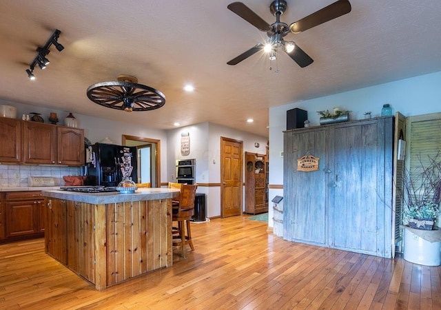 kitchen featuring a kitchen breakfast bar, black refrigerator with ice dispenser, light hardwood / wood-style flooring, decorative backsplash, and a kitchen island