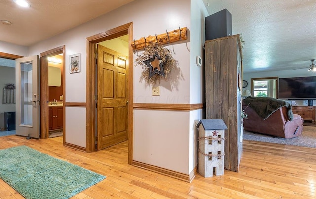 corridor with sink, a textured ceiling, and light hardwood / wood-style flooring