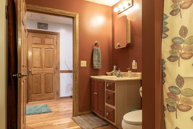 bathroom with walk in shower, hardwood / wood-style floors, vanity, and toilet