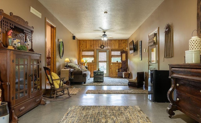 interior space with a textured ceiling, ceiling fan, concrete floors, and wood walls