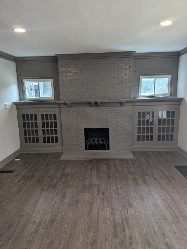 unfurnished living room with dark hardwood / wood-style floors, ornamental molding, brick wall, and a brick fireplace