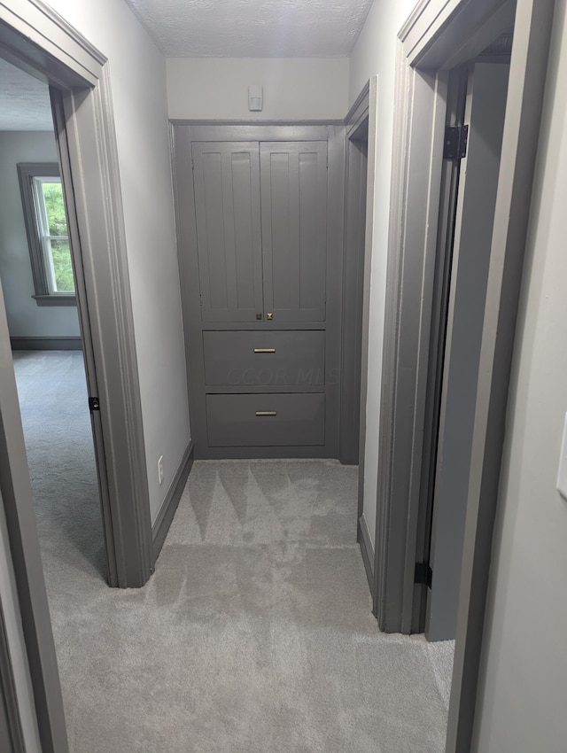 hallway featuring light colored carpet and a textured ceiling