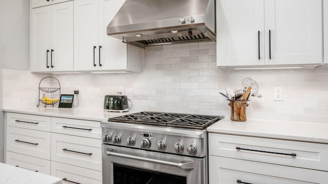 kitchen with white cabinetry, high end stove, wall chimney range hood, and tasteful backsplash