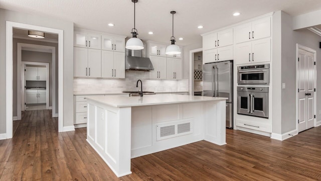 kitchen featuring wall chimney range hood, sink, hanging light fixtures, white cabinetry, and stainless steel appliances