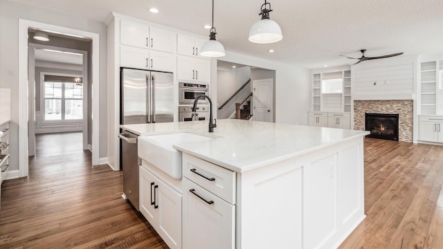 kitchen featuring a center island with sink, white cabinets, hanging light fixtures, ceiling fan, and stainless steel appliances