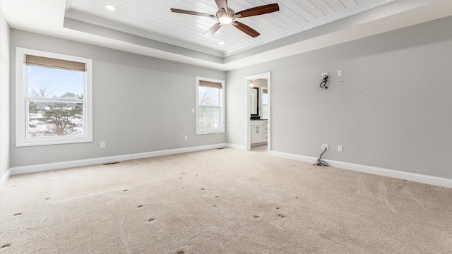 empty room with a raised ceiling, light carpet, crown molding, and ceiling fan