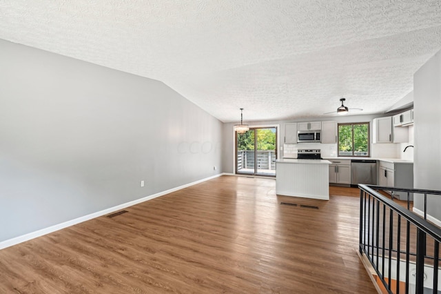 kitchen with appliances with stainless steel finishes, a textured ceiling, pendant lighting, hardwood / wood-style flooring, and gray cabinets