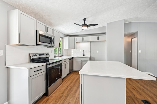 kitchen with ceiling fan, backsplash, appliances with stainless steel finishes, a kitchen island, and light wood-type flooring