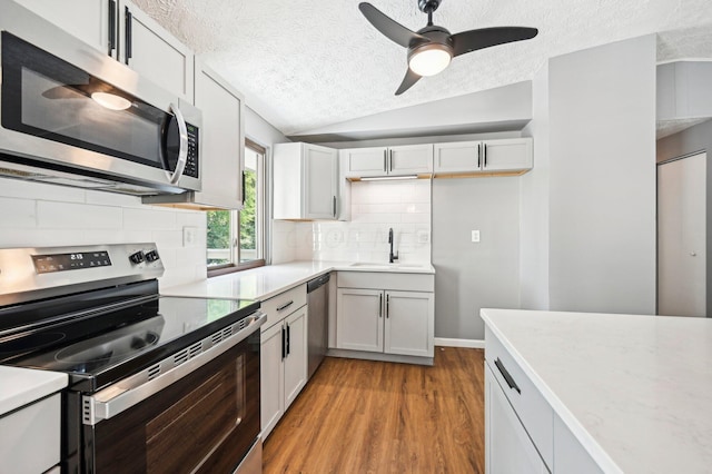 kitchen featuring a textured ceiling, stainless steel appliances, vaulted ceiling, sink, and light hardwood / wood-style flooring