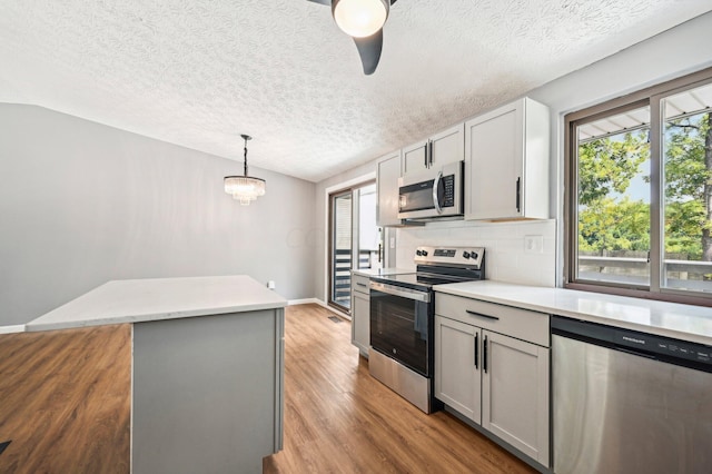 kitchen with appliances with stainless steel finishes, light wood-type flooring, vaulted ceiling, gray cabinets, and hanging light fixtures