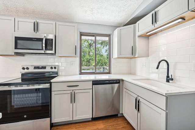 kitchen with sink, tasteful backsplash, hardwood / wood-style floors, a textured ceiling, and appliances with stainless steel finishes