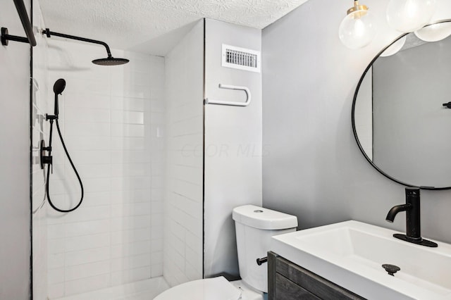 bathroom featuring vanity, toilet, tiled shower, and a textured ceiling