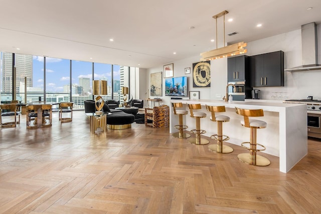 kitchen with a breakfast bar, light parquet floors, a center island with sink, wall chimney exhaust hood, and stainless steel appliances