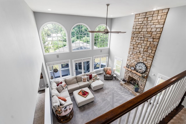 carpeted living room with ceiling fan, a fireplace, and a towering ceiling