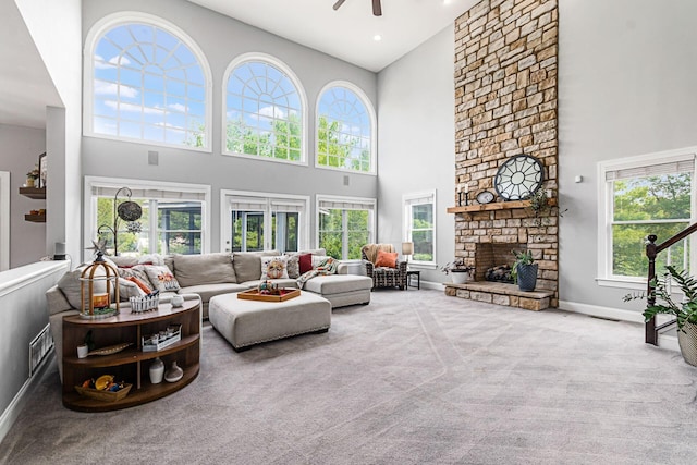 carpeted living room featuring a stone fireplace, ceiling fan, a towering ceiling, and a healthy amount of sunlight