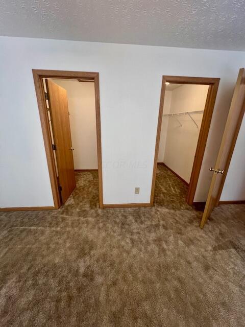 unfurnished bedroom with a spacious closet, a textured ceiling, dark carpet, and a closet