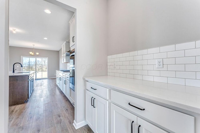 kitchen featuring tasteful backsplash, white cabinets, light stone counters, and decorative light fixtures