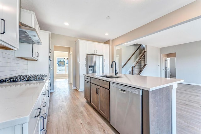 kitchen featuring a kitchen island with sink, ventilation hood, white cabinets, and appliances with stainless steel finishes