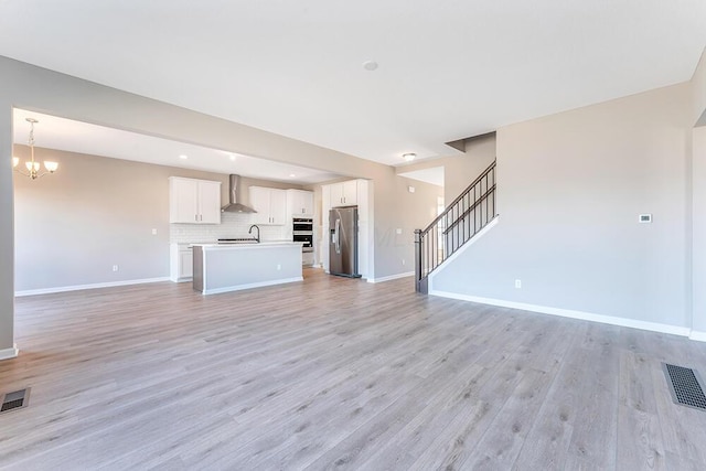 unfurnished living room with an inviting chandelier, sink, and light wood-type flooring