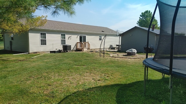 rear view of house with central AC, a yard, and a trampoline