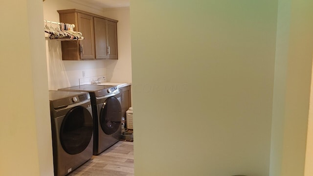 laundry area with sink, washer and clothes dryer, cabinets, and light wood-type flooring