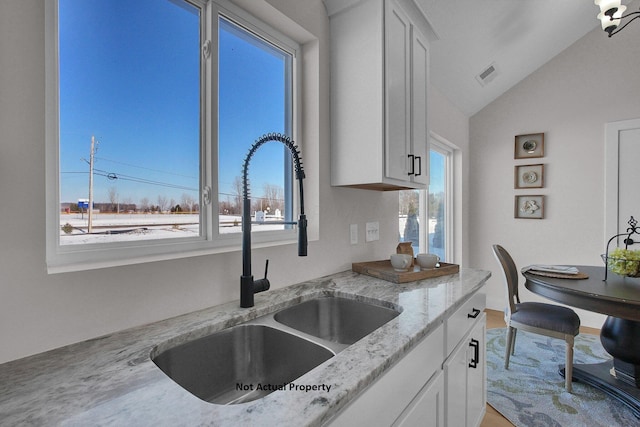 kitchen with vaulted ceiling, white cabinetry, sink, and light stone countertops