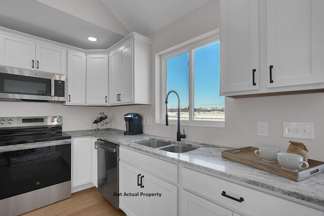 kitchen with appliances with stainless steel finishes, vaulted ceiling, white cabinets, light stone counters, and sink