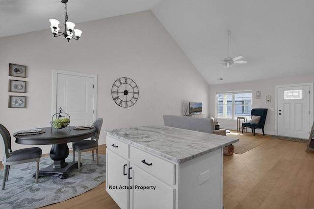 kitchen with pendant lighting, light wood-type flooring, high vaulted ceiling, white cabinets, and ceiling fan with notable chandelier