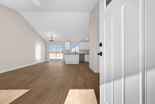 unfurnished living room featuring vaulted ceiling, ceiling fan with notable chandelier, hardwood / wood-style flooring, and sink