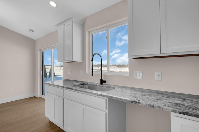 kitchen featuring light wood-type flooring, white cabinetry, light stone counters, and sink