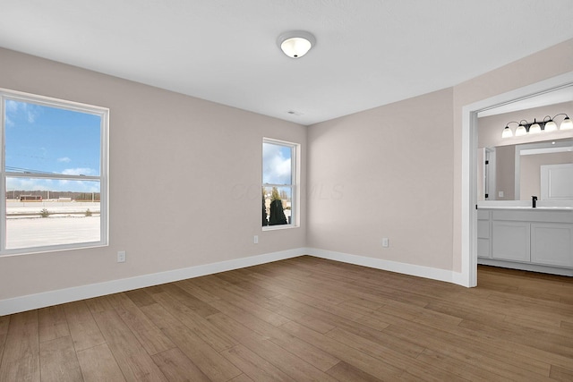 unfurnished bedroom with ensuite bath, wood-type flooring, and sink