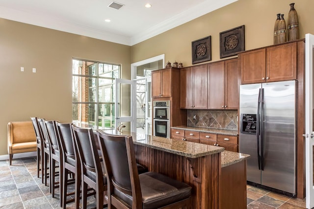 kitchen featuring light stone countertops, a center island, decorative backsplash, a breakfast bar, and appliances with stainless steel finishes