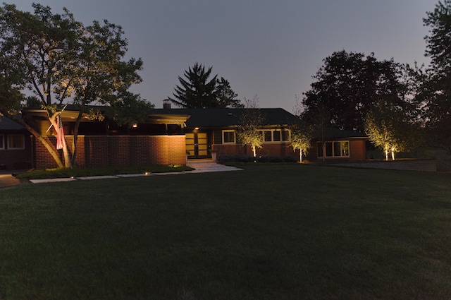 back of property at dusk with a yard and brick siding