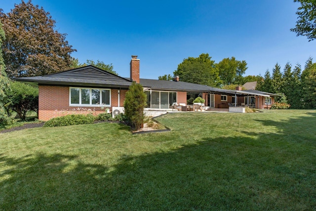 rear view of house with brick siding, a patio area, a chimney, and a yard