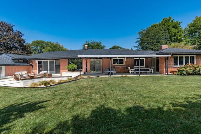 rear view of house featuring brick siding, a patio, a chimney, and a yard