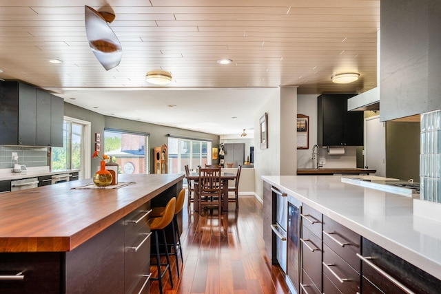 kitchen with recessed lighting, dark wood-style flooring, decorative backsplash, a kitchen bar, and butcher block counters