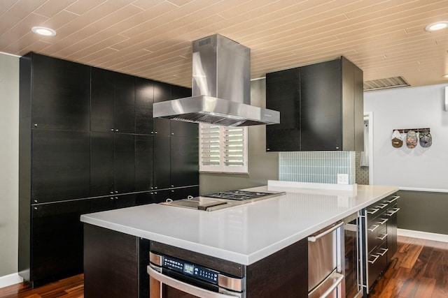 kitchen featuring island exhaust hood, dark wood-style floors, dark cabinetry, stainless steel appliances, and light countertops