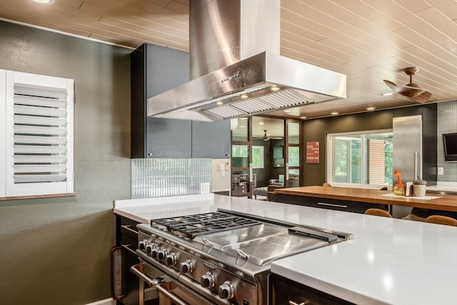 kitchen featuring ceiling fan, high end stove, wall chimney exhaust hood, and a textured wall