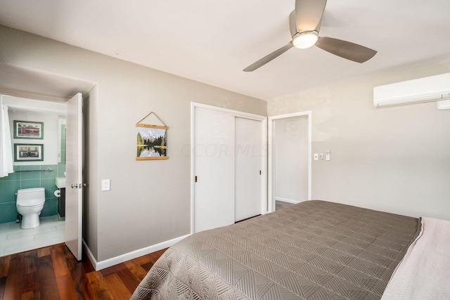 bedroom with a ceiling fan, wood finished floors, baseboards, a closet, and a wall mounted air conditioner