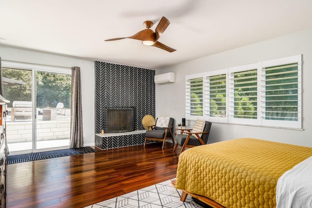 bedroom with access to outside, wood finished floors, a wall unit AC, an accent wall, and a tile fireplace