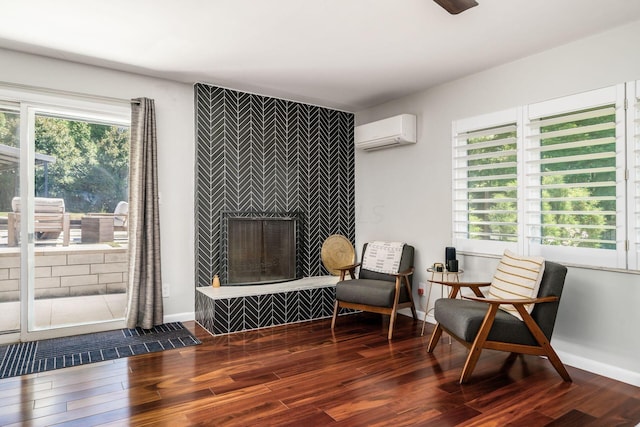 living area featuring a wall unit AC, wood finished floors, a fireplace, and baseboards