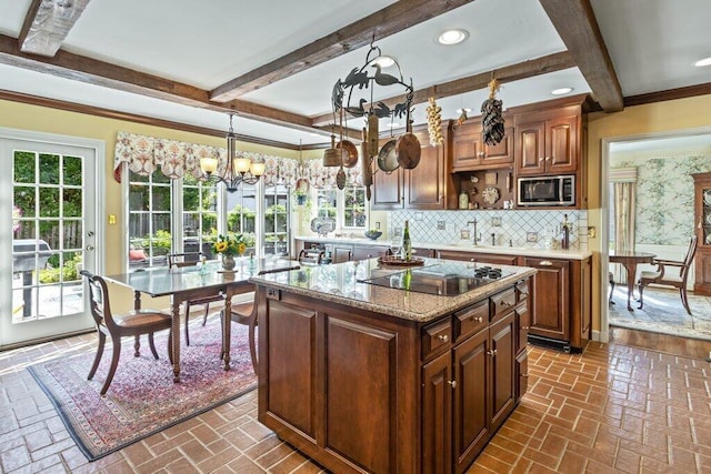 kitchen with a center island, stainless steel microwave, an inviting chandelier, black electric cooktop, and decorative light fixtures