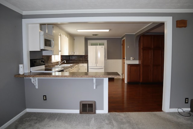 kitchen featuring sink, kitchen peninsula, crown molding, white appliances, and dark carpet