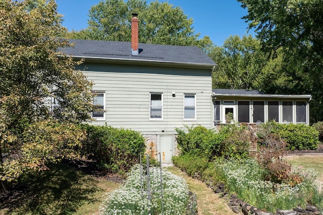 back of house with a sunroom, a chimney, and roof with shingles