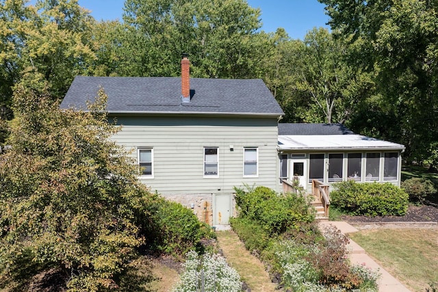 rear view of house with a shingled roof, a chimney, and a sunroom